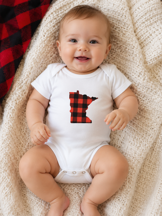 Baby wearing a white onesie with a red and black checkered MN on a beige blanket.