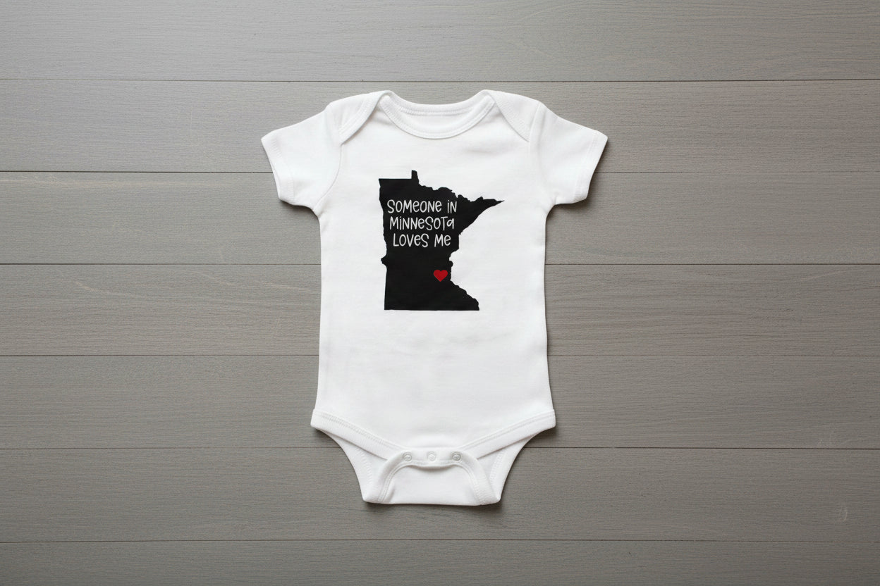 White baby onesie with a black outline of Minnesota and text 'Someone in Minnesota loves me' 